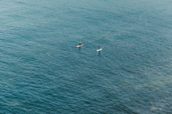 Two paddleboarders on turquoise water beside white cliffs
